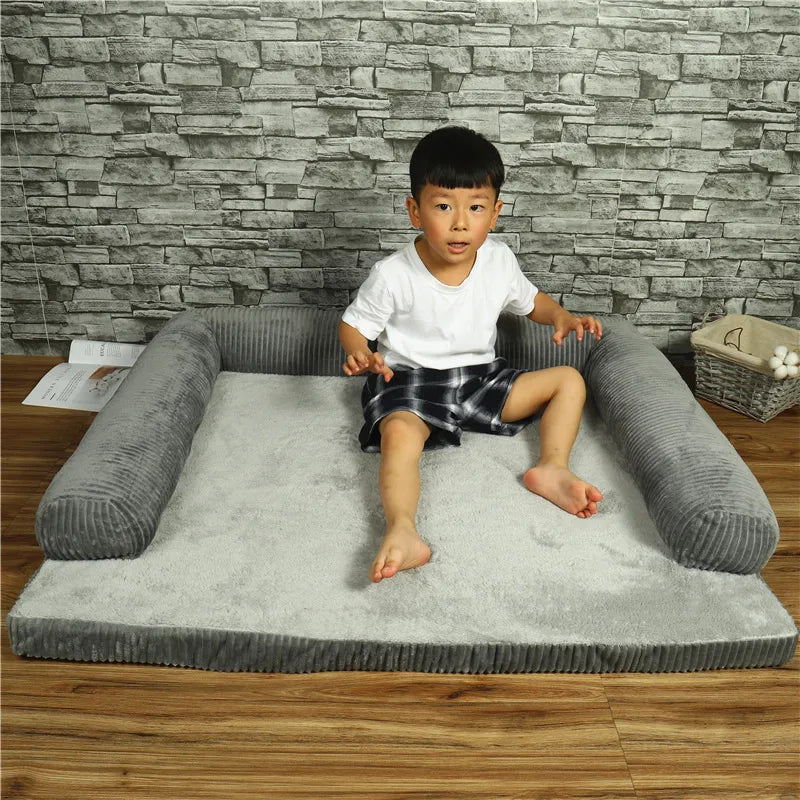 Child sitting on a gray pet bed against a stone wall.