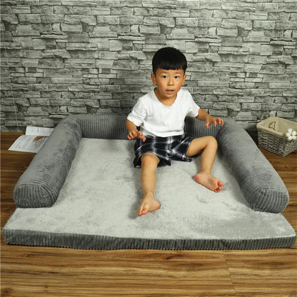Child sitting on a gray pet bed against a stone wall.